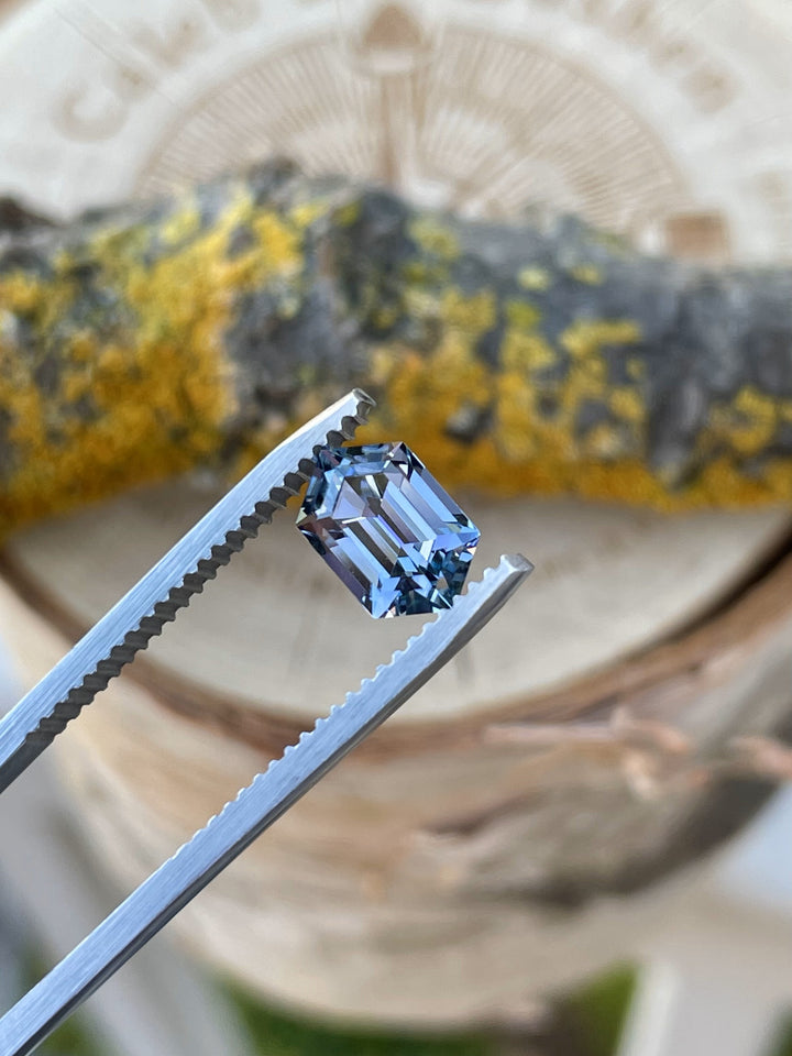 Close-up of a 1.60ct blue and violet Tanzanite in step cut hexagon shape held by gem tweezers