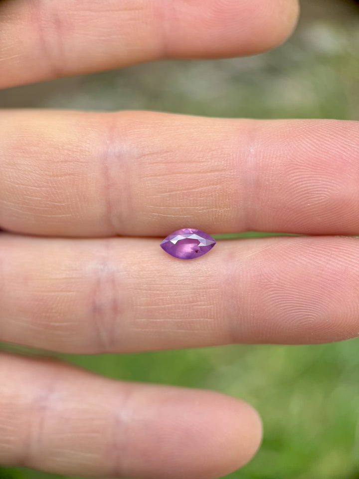 Marquise-cut 1.15CT sapphire with violet and opalescent pink tones displayed on fingertips, showcasing brilliance and luster