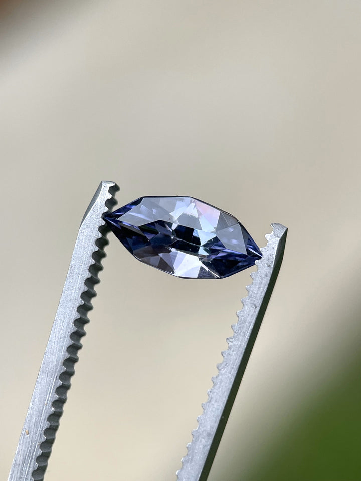 Tanzanite held in tweezers against a soft background, revealing its deep violet and purple coloration in a sharp custom marquise shape.