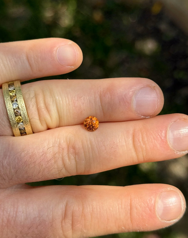 1.11 carat round brilliant Hessonite garnet held between fingers showing yellow-orange glow