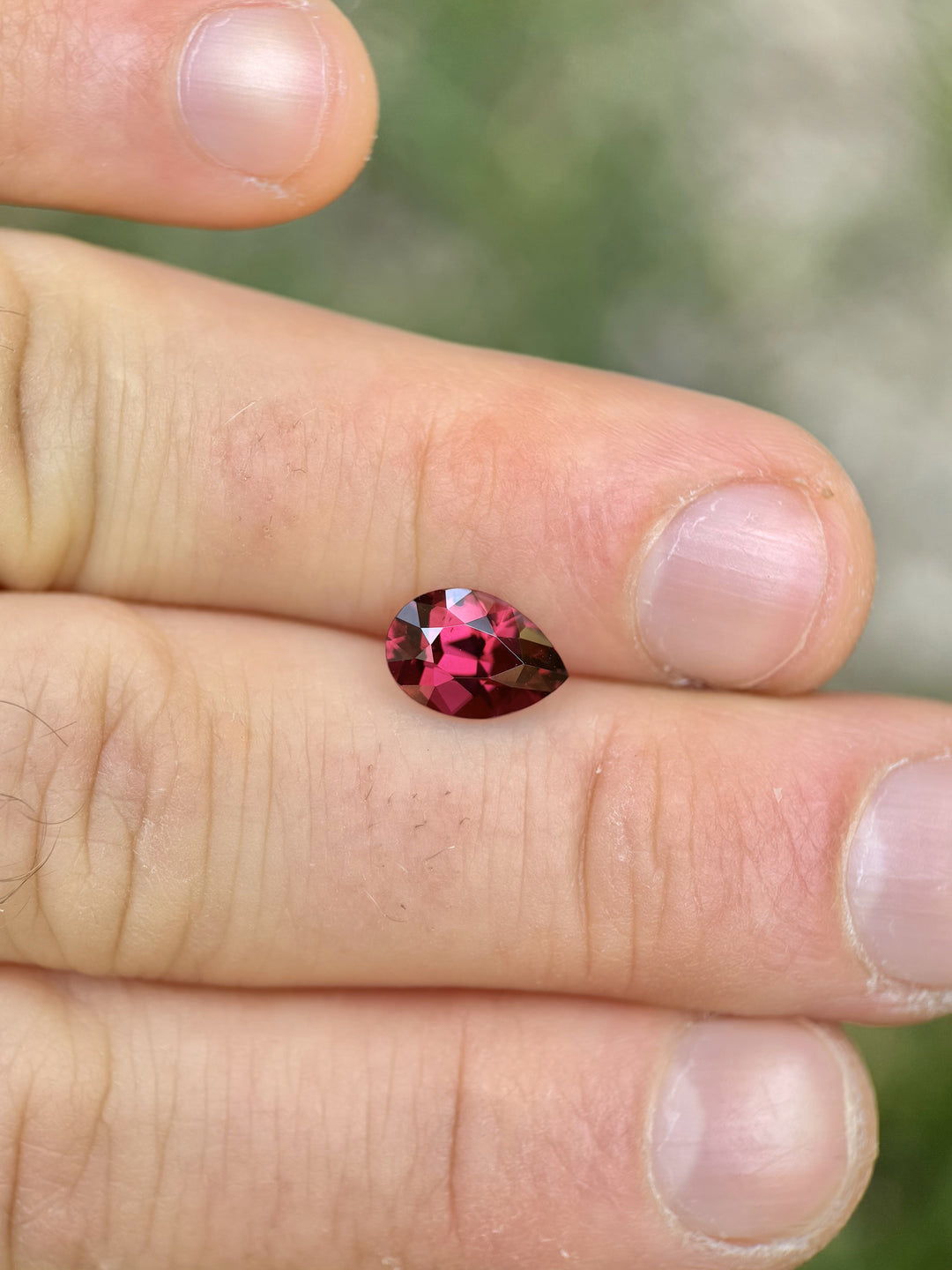 2.40 carat raspberry red garnet in precision poval cut displayed between fingers, showcasing its vibrant color and brilliance