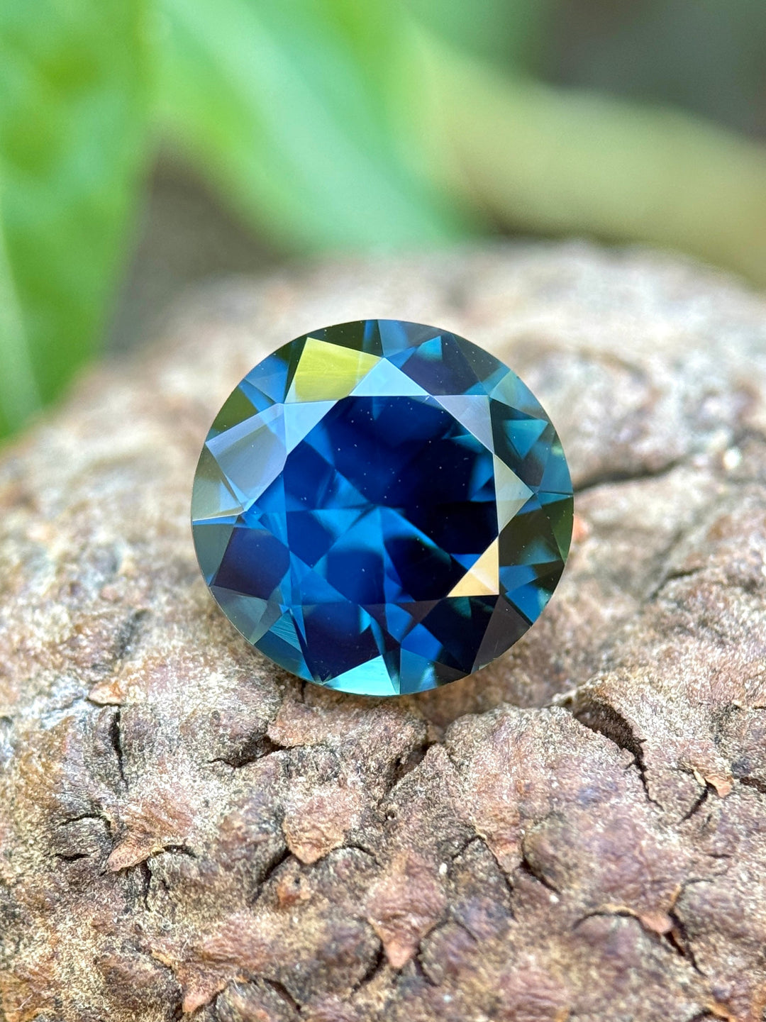 3.98 carat vivid peacock teal blue green sapphire resting on natural stone, round brilliant cut sapphire from Gombe Nigeria showing deep saturation and crisp faceting