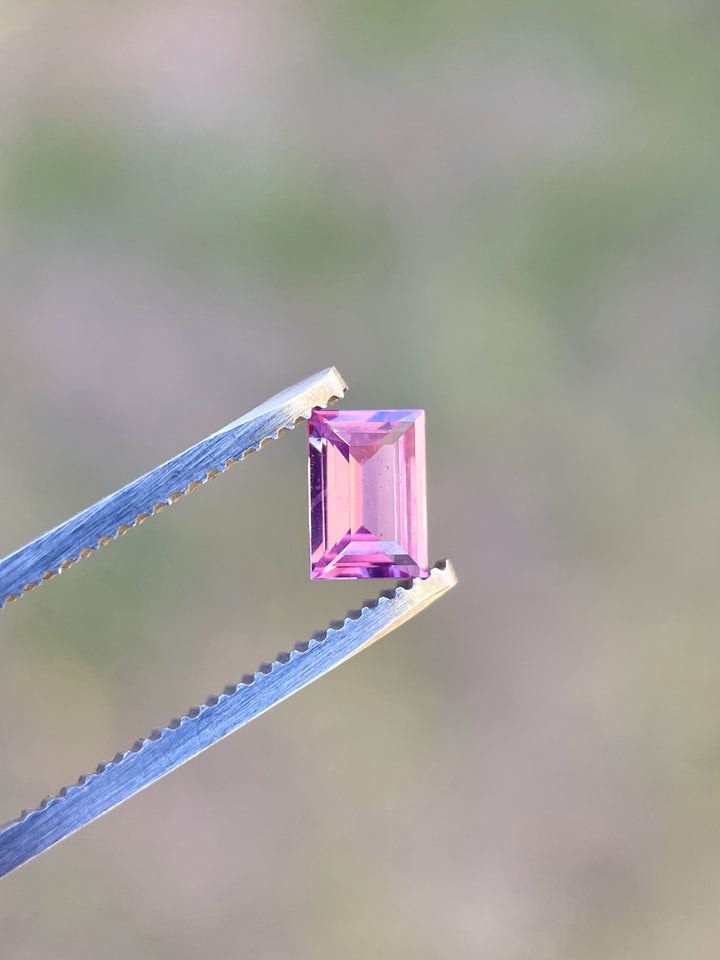 Close-up view of a 1.10 carat sapphire, showcasing its emerald cut and vibrant color spectrum of pink, purple, and mulberry, elegantly placed on a neutral background.