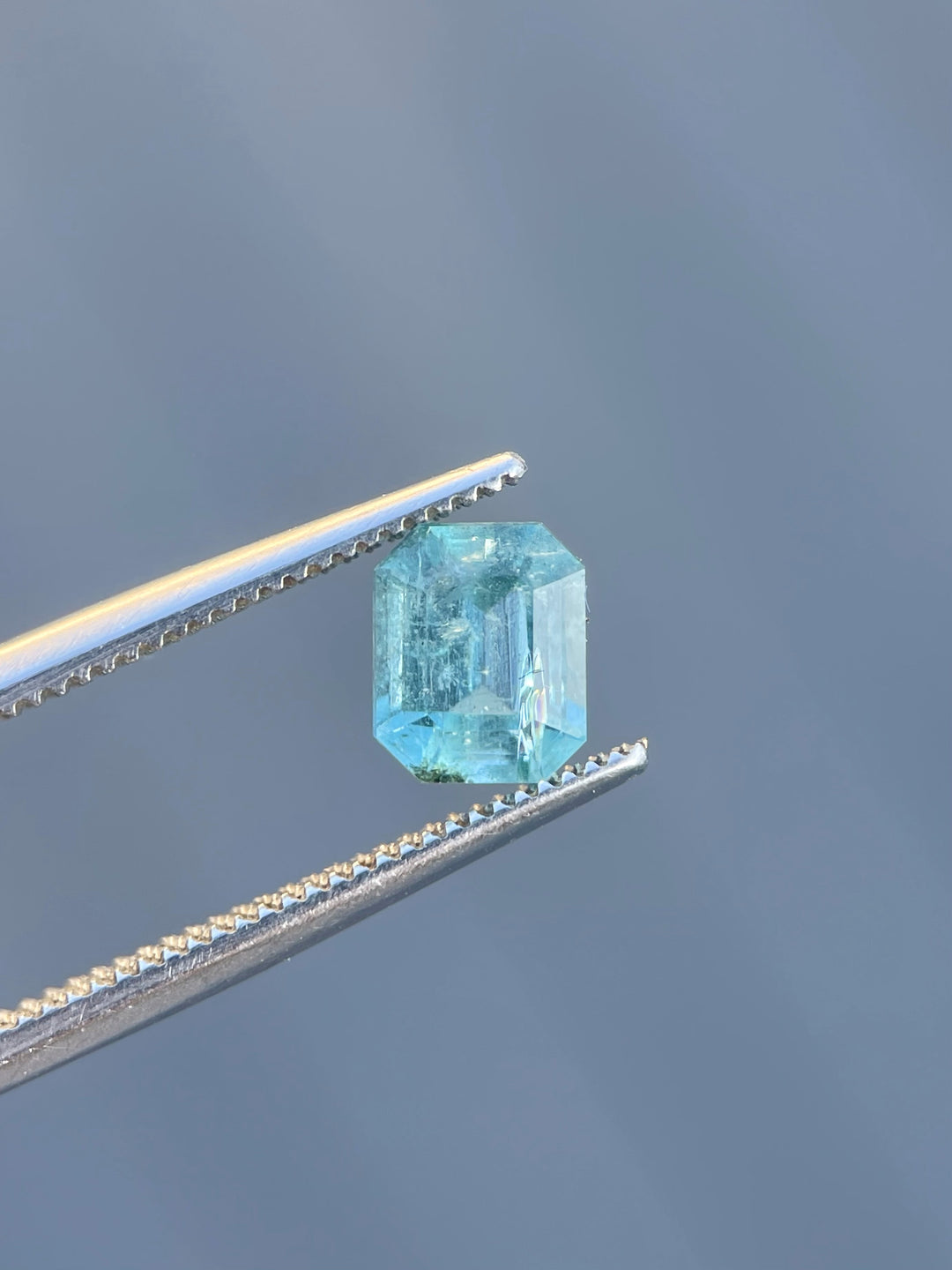 A 1.17-carat emerald gemstone, emerald cut, with vibrant green-blue hues held in precision tweezers.