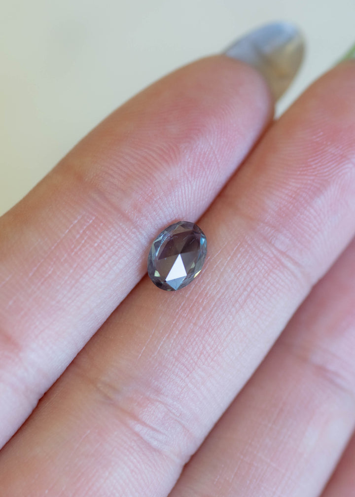 Faceted teal rose cut sapphire held between two fingers on a light background