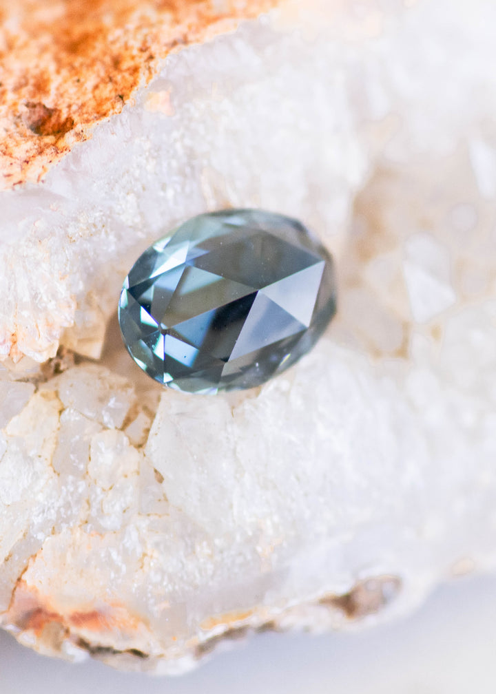 Natural Madagascar sapphire showing deep teal and blue-green color zoning with rose-cut faceting reflected across the gemstone's surface.