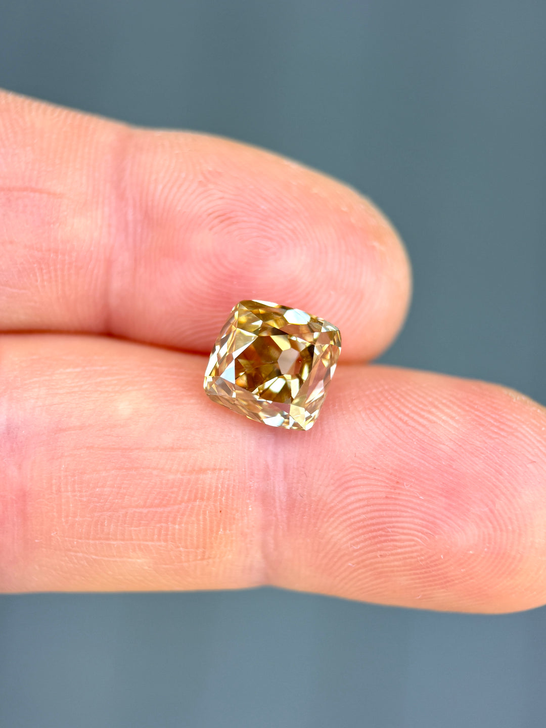 Close-up of a 5.21ct Fancy Brown C5 Diamond held on fingertips highlighting its old mine cushion shape, vintage facet pattern, and luxurious cognac-champagne brilliance.