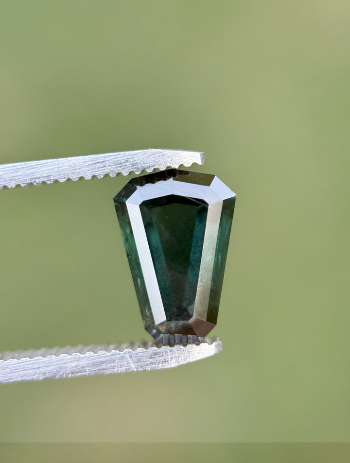 3.65ct custom shield-cut sapphire from Kenya showing deep peacock tones with teal, green, and blue flashes.