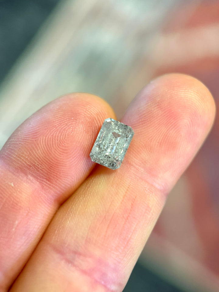 A rectangular emerald-cut diamond held between two fingers to show its small scale.