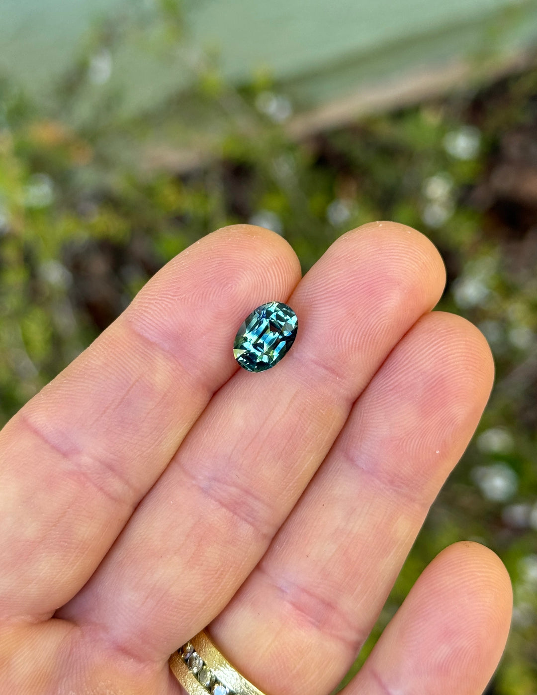 Person holding a blue gemstone between their fingers with a blurred natural background