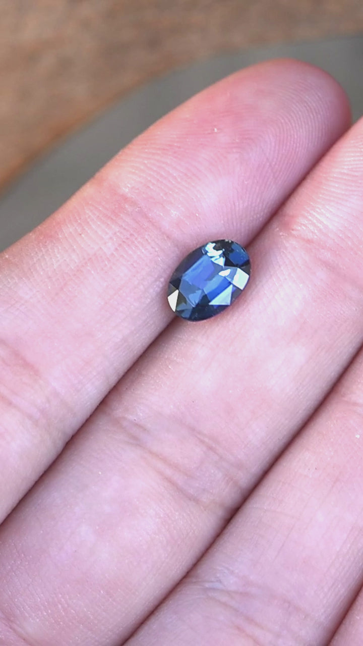 2.29ct Deep oceanic blue oval mix cut sapphire rotating in finger tips under natural light.