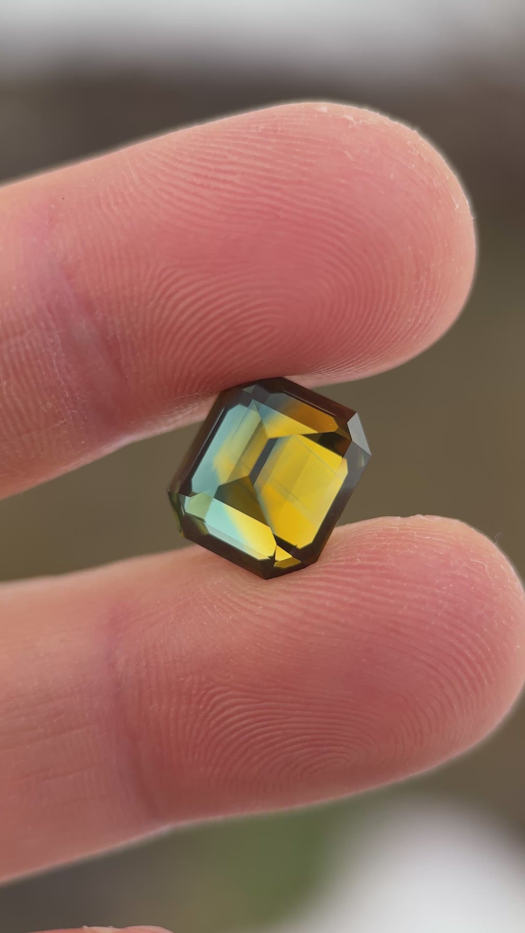 Close-up video of a 9.14ct Nigerian parti sapphire emerald cut, slowly moving under light to display vivid orange, yellow, blue, and green color zoning and exceptional clarity from Gombe, Nigeria