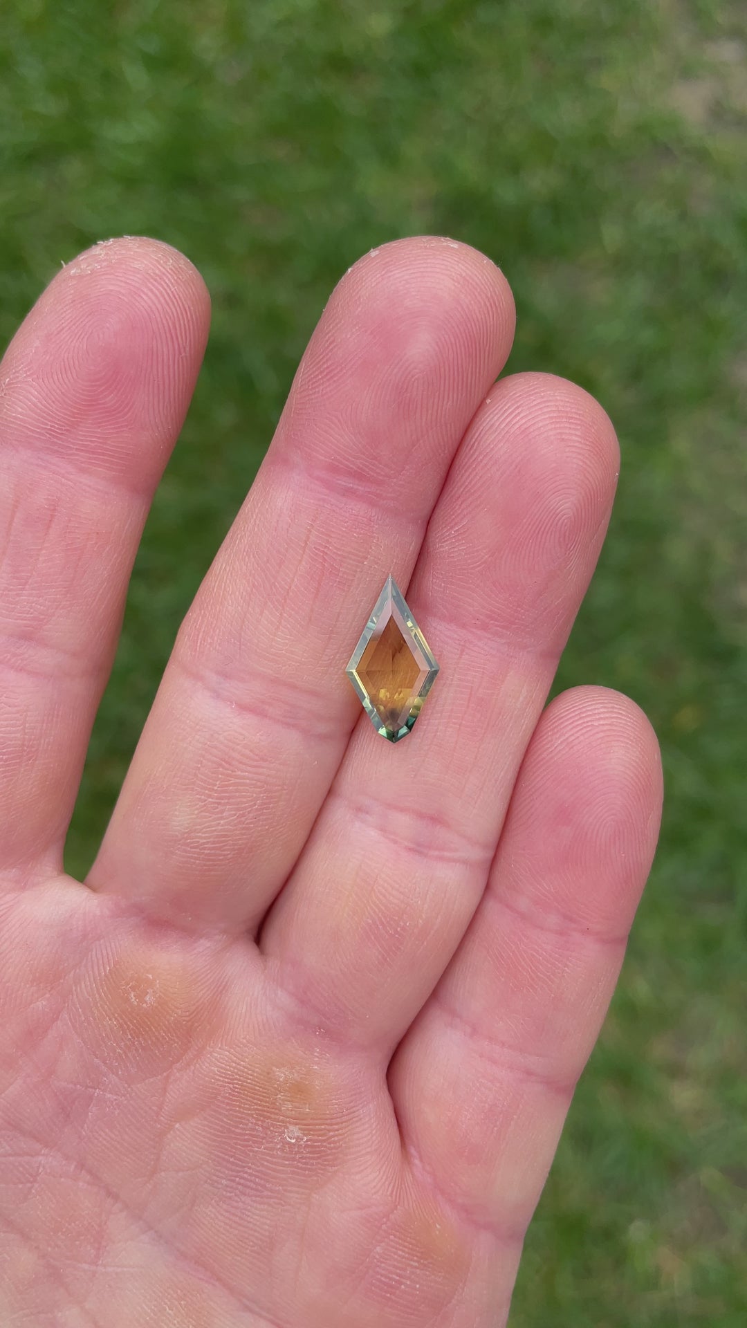 Handheld video showcasing a 2.38-carat kite-shaped parti sapphire from Kenya, revealing color zoning between yellow and blue in natural light.