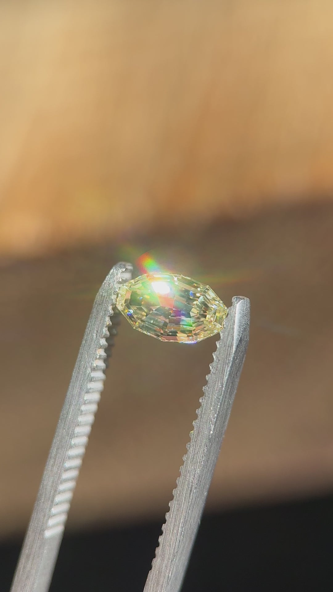 Handheld video of a 0.99 carat light yellow VVS1 diamond from Gahcho Kué, Canada, gently moved in tweezers to reveal the brilliance and intricate symmetry of its antique moval step cut under natural light.