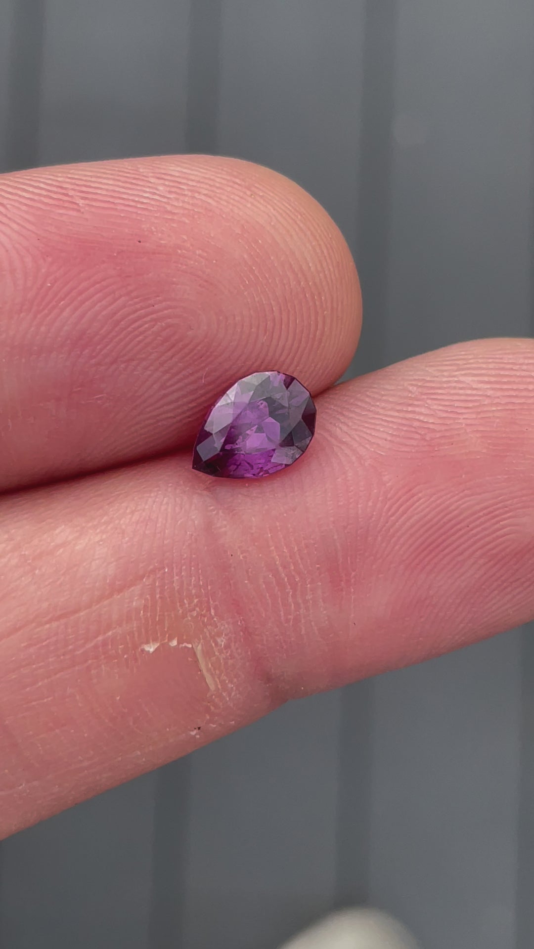 A close-up video of the pinkish-purple pear-shaped sapphire placed on a textured surface, displaying its sparkle and facets.