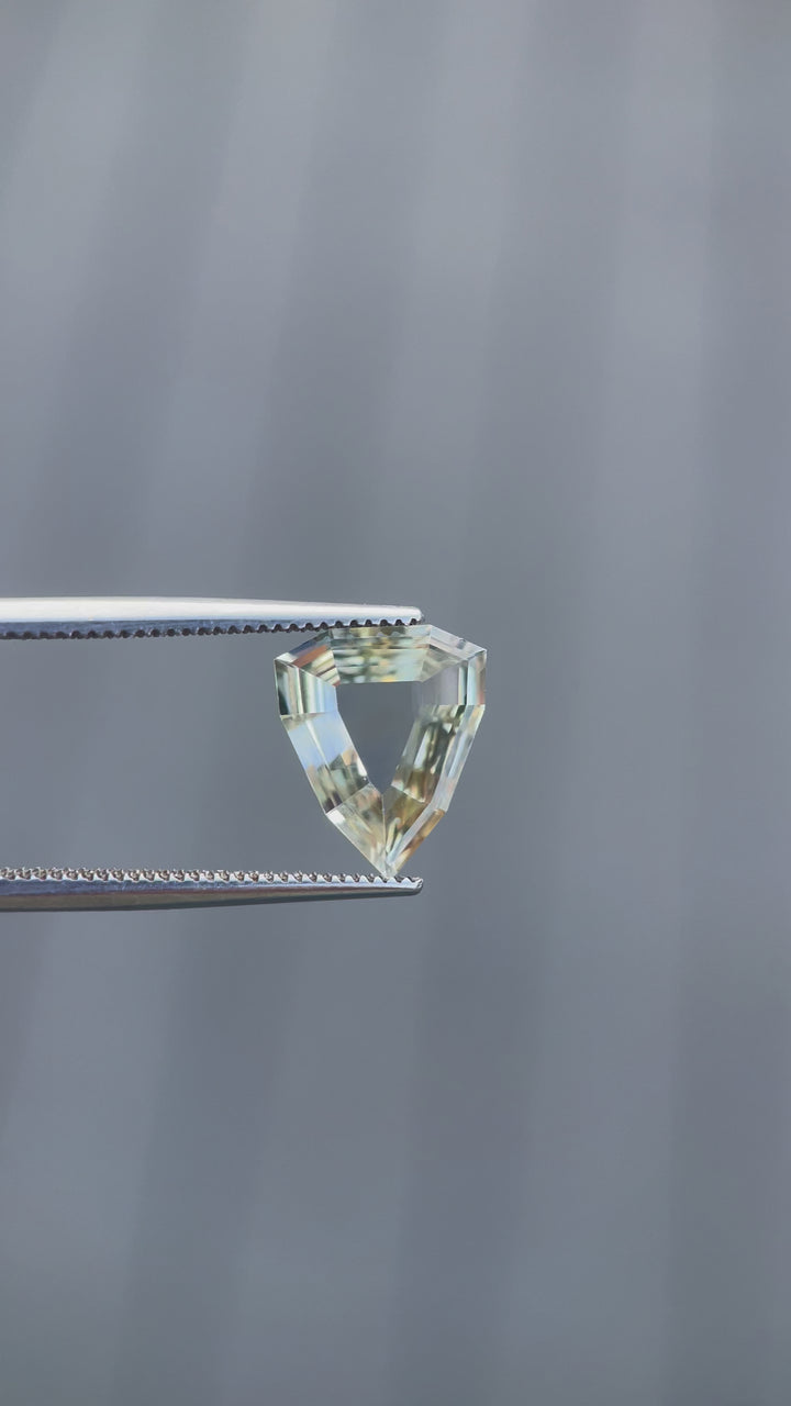 A rotating 2.47-carat yellow-green sapphire with a modified geometric step cut. The video showcases the precision of the portrait shield shape as the light interacts with its facets. The untreated sapphire from Sri Lanka measures 11.68mm by 9.62mm by 2.63mm.