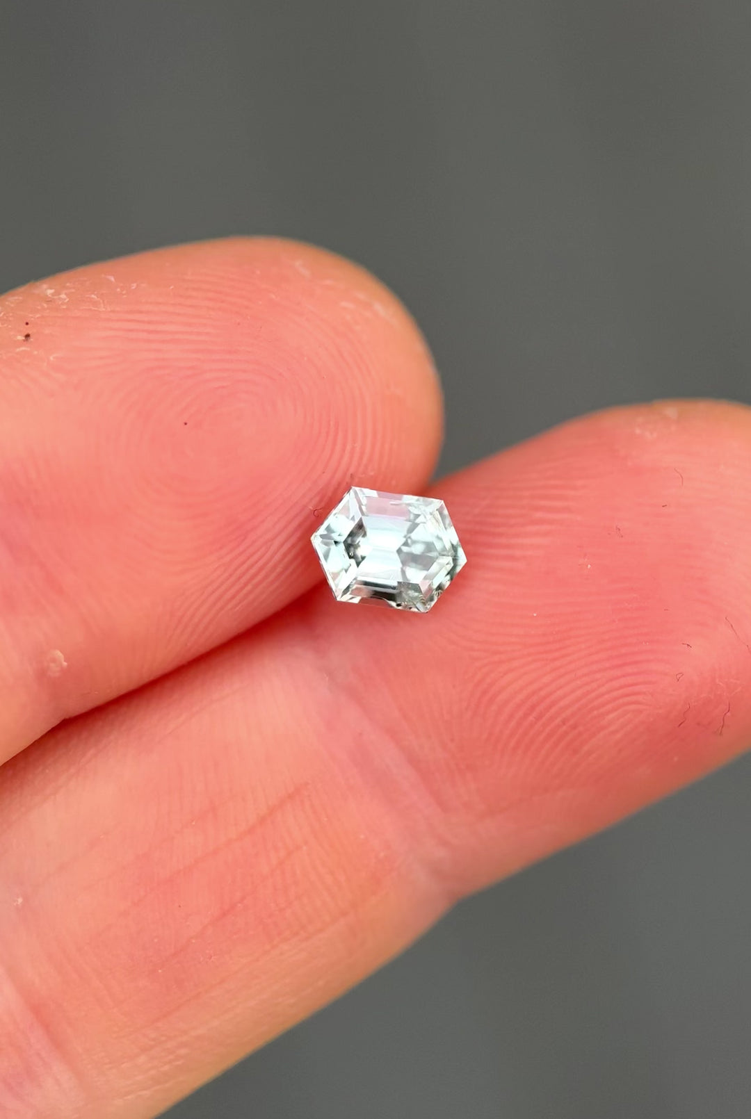 Handheld video showcasing an untreated Montana sapphire as it moves through light, demonstrating seafoam green to grey silver color shift, elongated hexagon step cut symmetry, and natural brilliance.