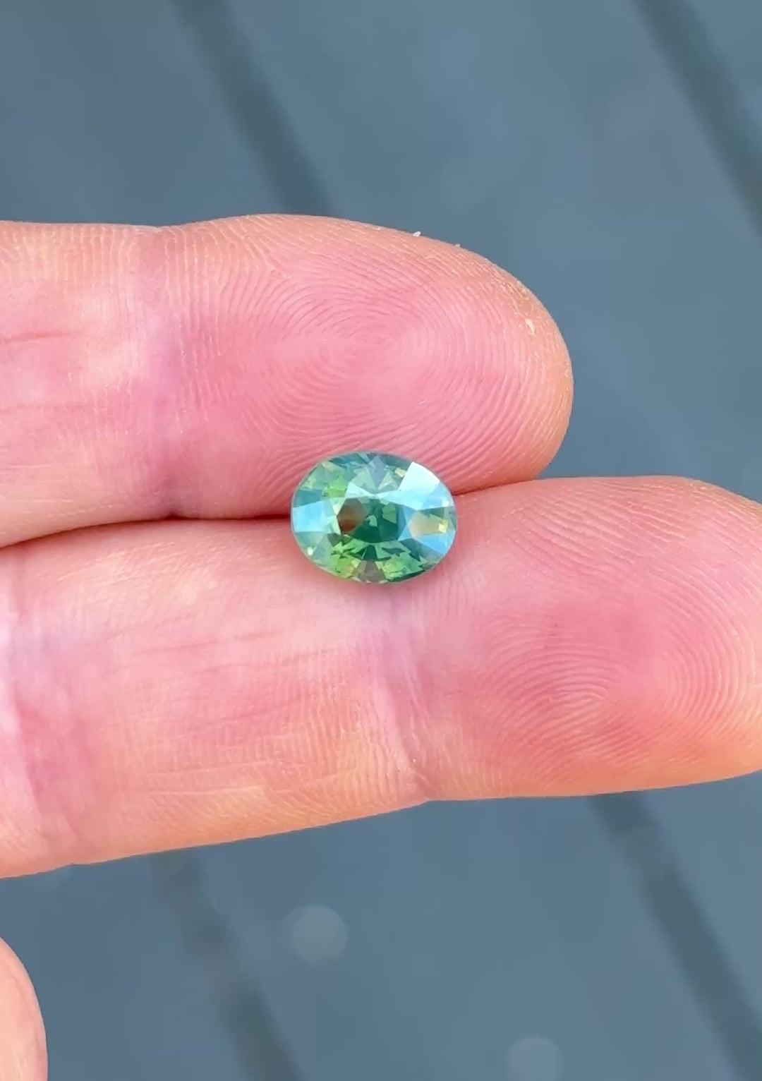 3.60ct opalescent teal blue green parti sapphire rotating in hand, revealing shifting ocean-inspired colors and bright precision-cut reflections.