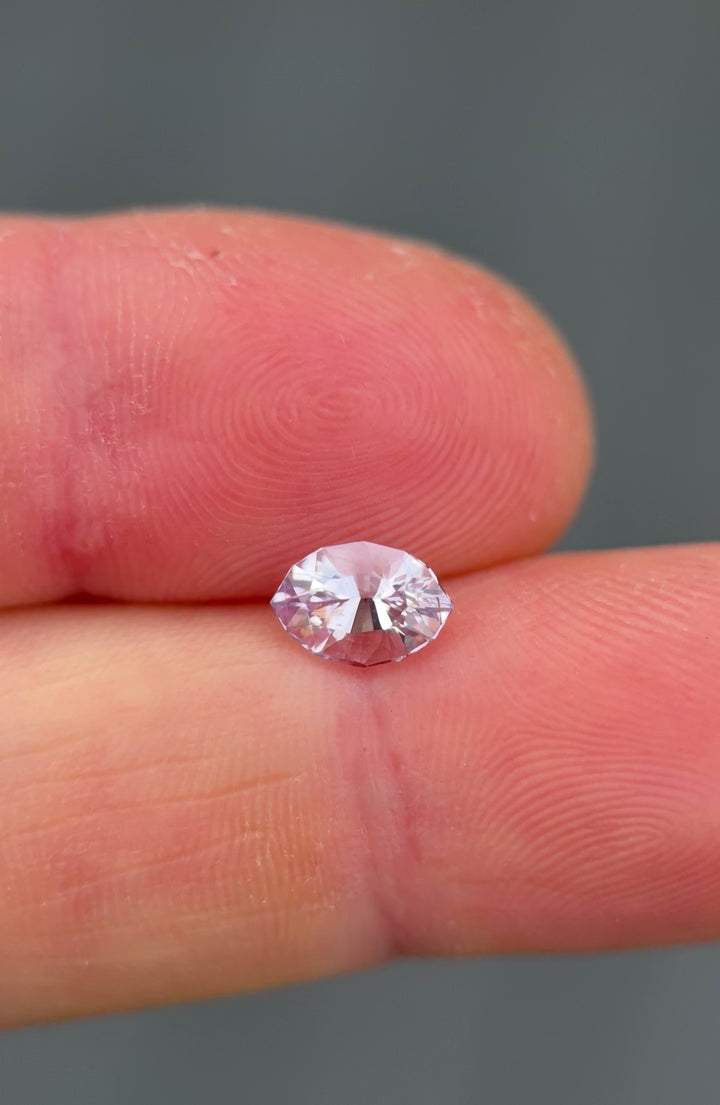 Macro video of 1.32 carat pink, purple, and lilac sapphire resting on fingertip, displaying light refraction, soft lilac tones, and intricate facet work of the precision marquise mixed cut, untreated sapphire from Sakaraha, Madagascar.