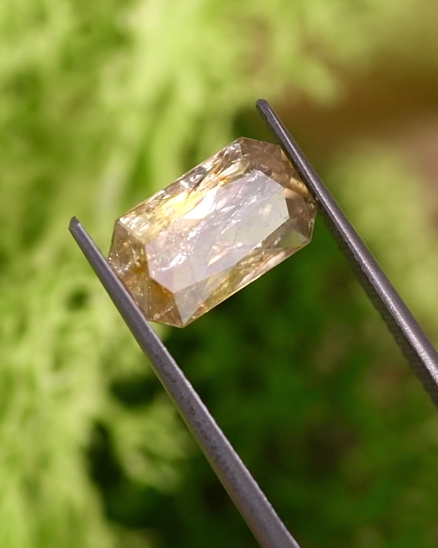 Video of 3.50CT yellow and orange sapphire turning in tweezers under natural sunlight, showing color shifts and sparkle through its custom modified radiant cut, untreated gemstone from Umba River Valley, Tanzania.