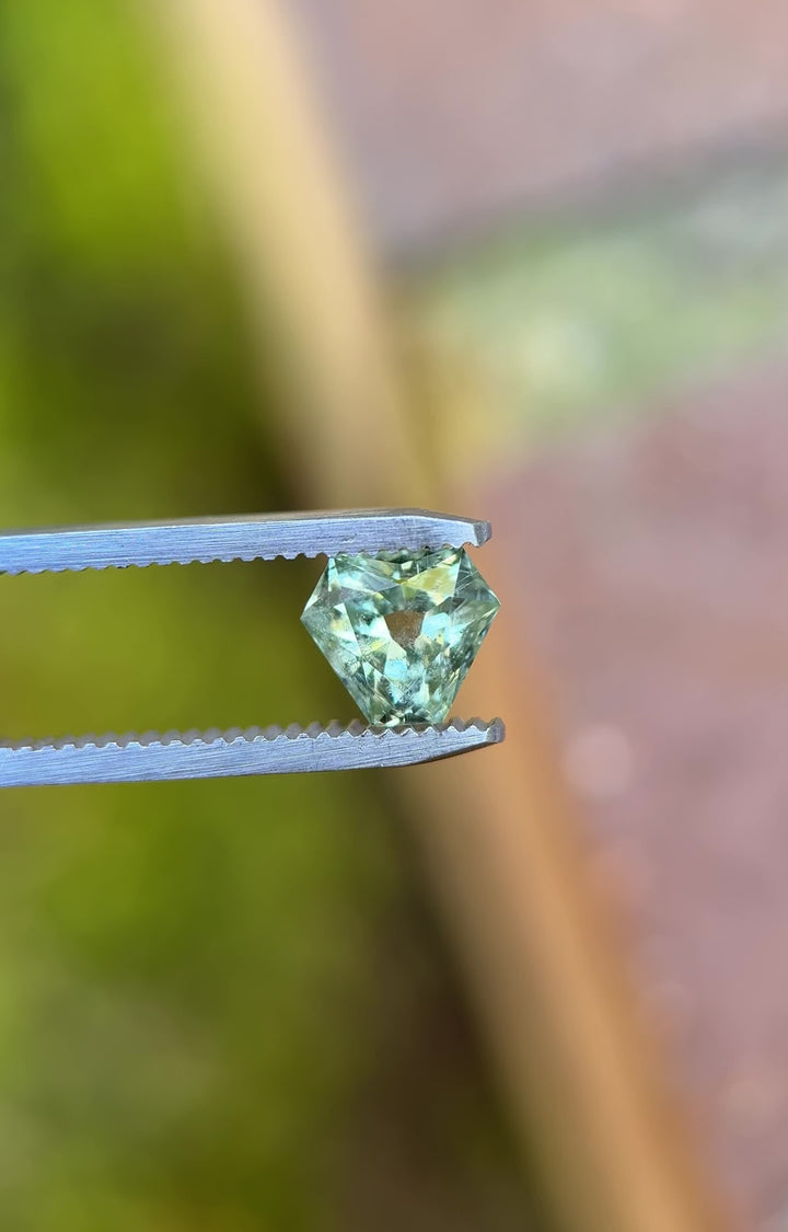 Video of a 1.90 carat mint teal green Montana sapphire rotating in tweezers, revealing antique style cut corner trillion facets, natural color zoning, and untreated brilliance