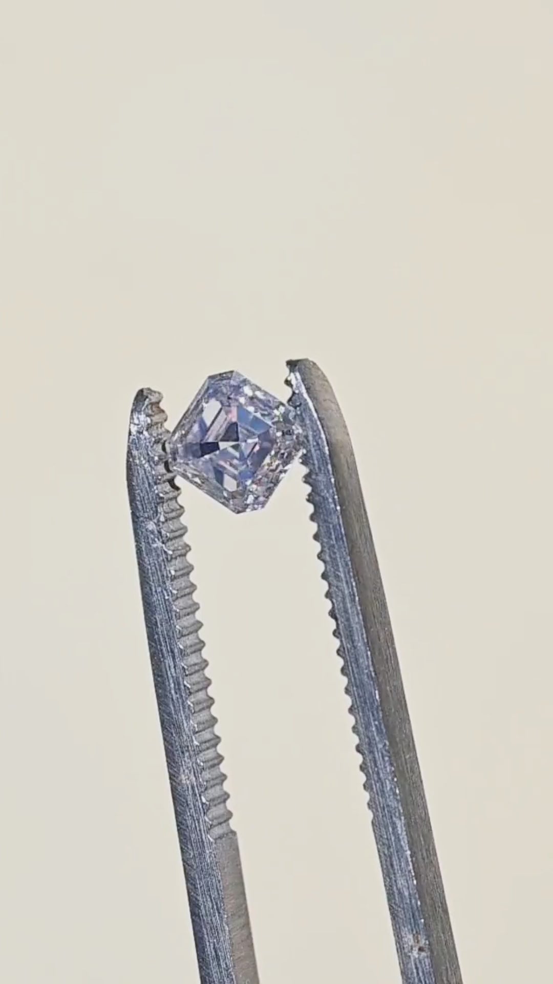 1.01 carat M color VVS1 Asscher cut diamond rotated in tweezers under sunlight, showing broad flashes of light across its concentric step facets.