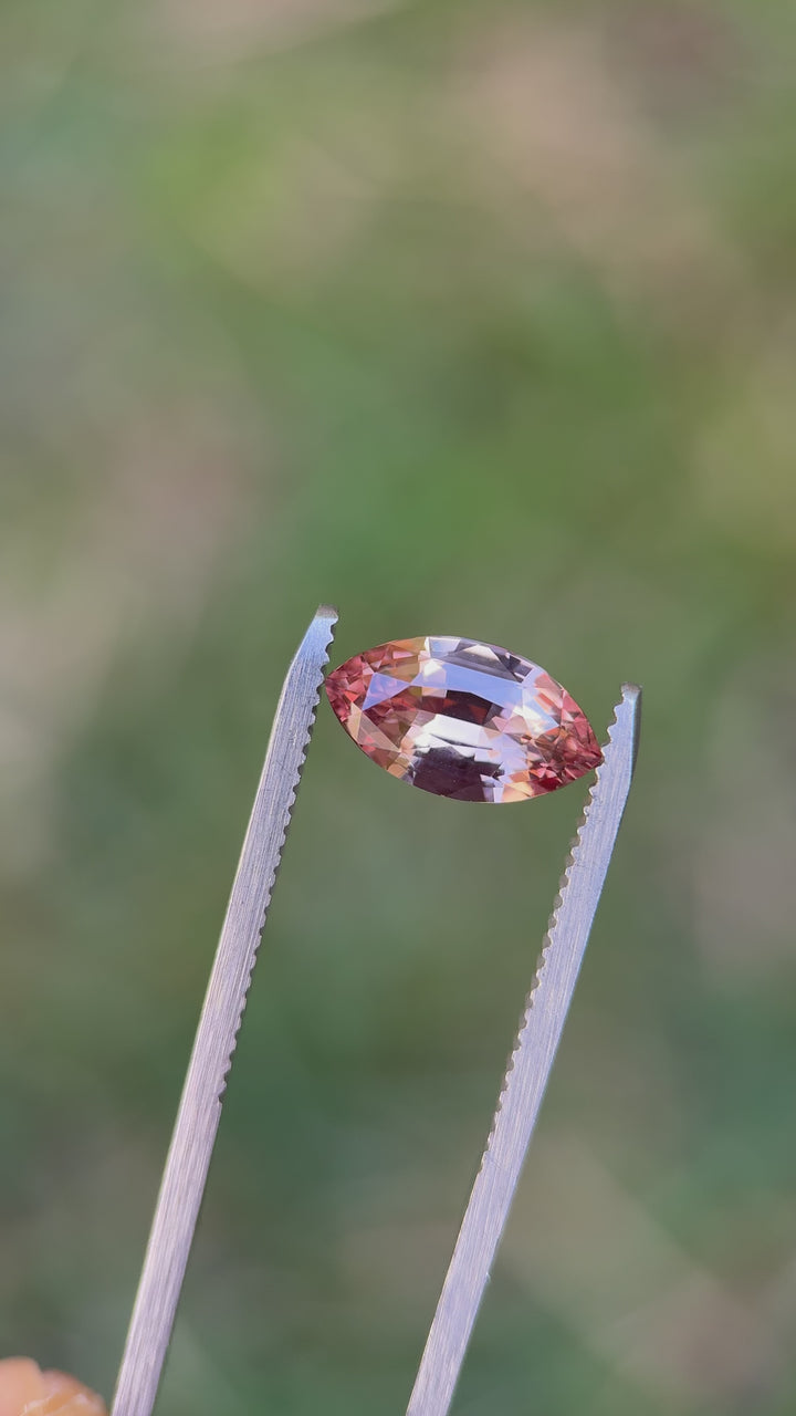 Video of a 2.57ct peach pink rose-champagne sapphire in a precision marquise mixed cut rotating in tweezers under natural light, showing sparkle, clarity, and color zoning; untreated sapphire from Sakaraha, Madagascar.