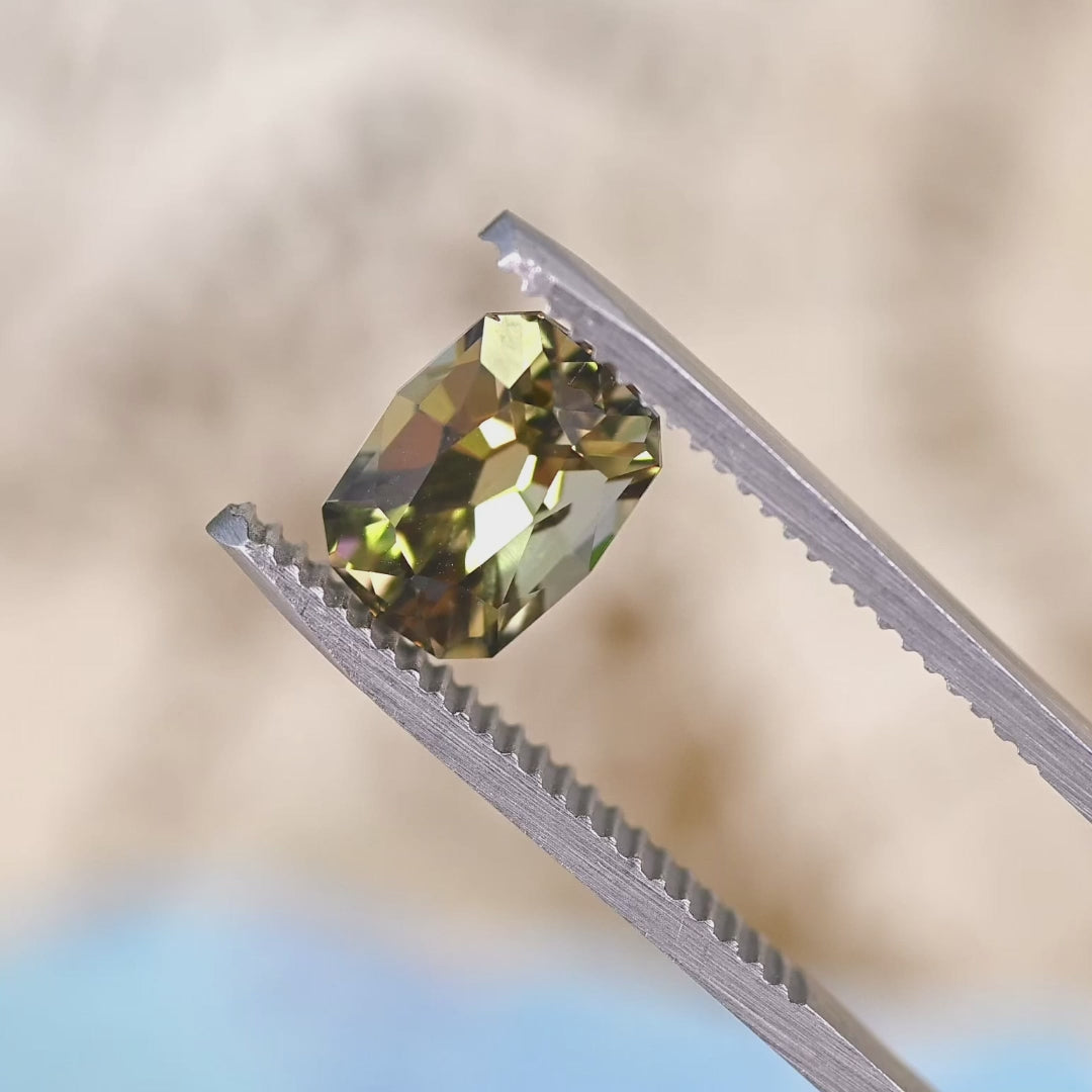 Close-up video of 2.59ct green yellow Tanzanite cushion cut held in tweezers, untreated custom faceted gemstone from Tanzania displaying clarity, sparkle and natural color