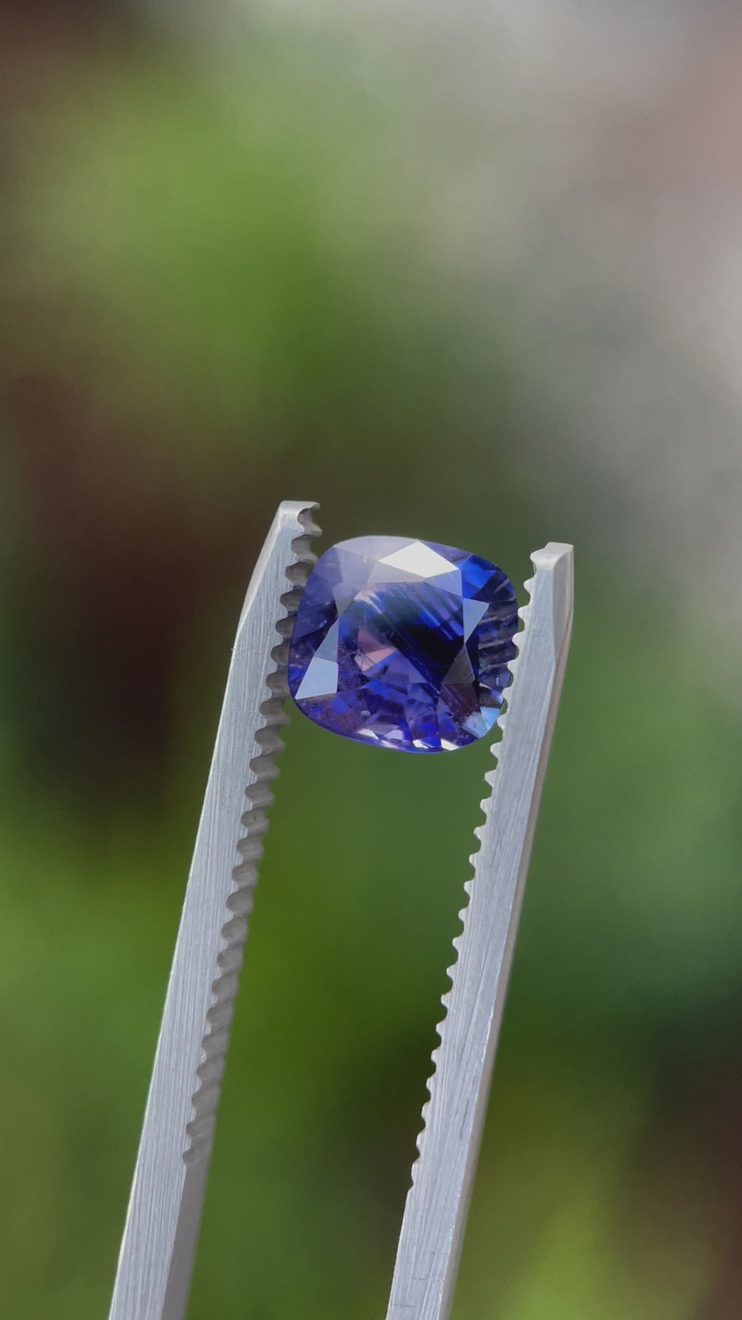 A detailed video of a smokey lavender and violet 1.82-carat sapphire being rotated in tweezers, showcasing its cushion cut and brilliant light reflection.