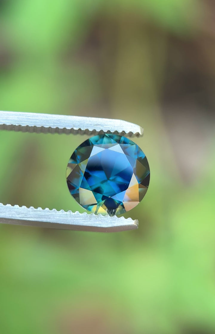 Video of a 3.98ct vivid peacock teal blue green sapphire rotating in tweezers, round brilliant cut Nigerian sapphire showing color shift, brilliance, and facet performance