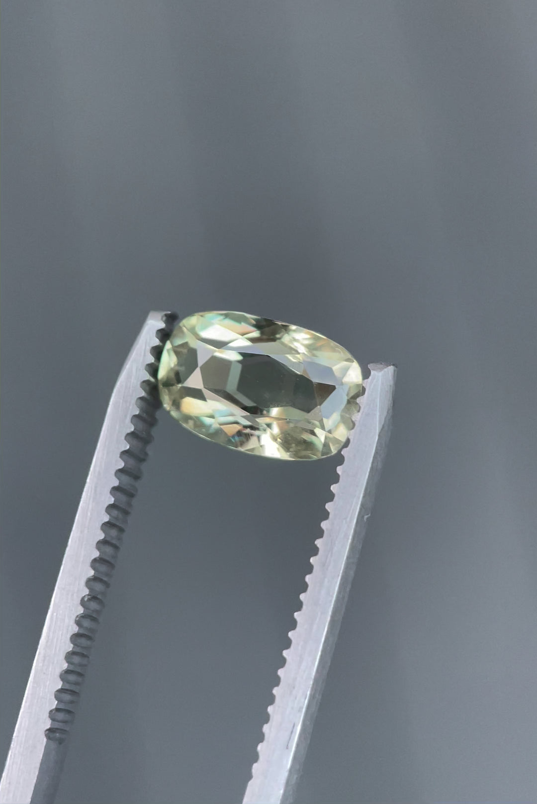 A detailed close-up of a 2.29-carat cushion-cut sapphire, reflecting beautiful shades of yellow, teal, and green. The gem is set against a natural background, emphasizing its vivid colors and luster. Origin: Umba River, Tanzania.