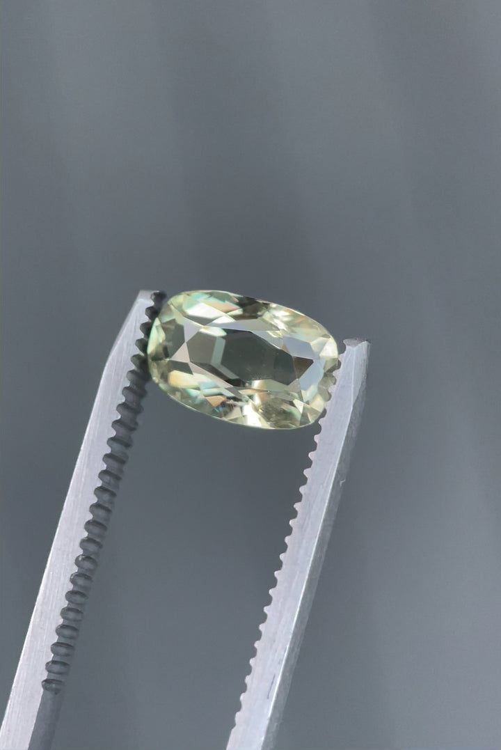 A detailed close-up of a 2.29-carat cushion-cut sapphire, reflecting beautiful shades of yellow, teal, and green. The gem is set against a natural background, emphasizing its vivid colors and luster. Origin: Umba River, Tanzania.
