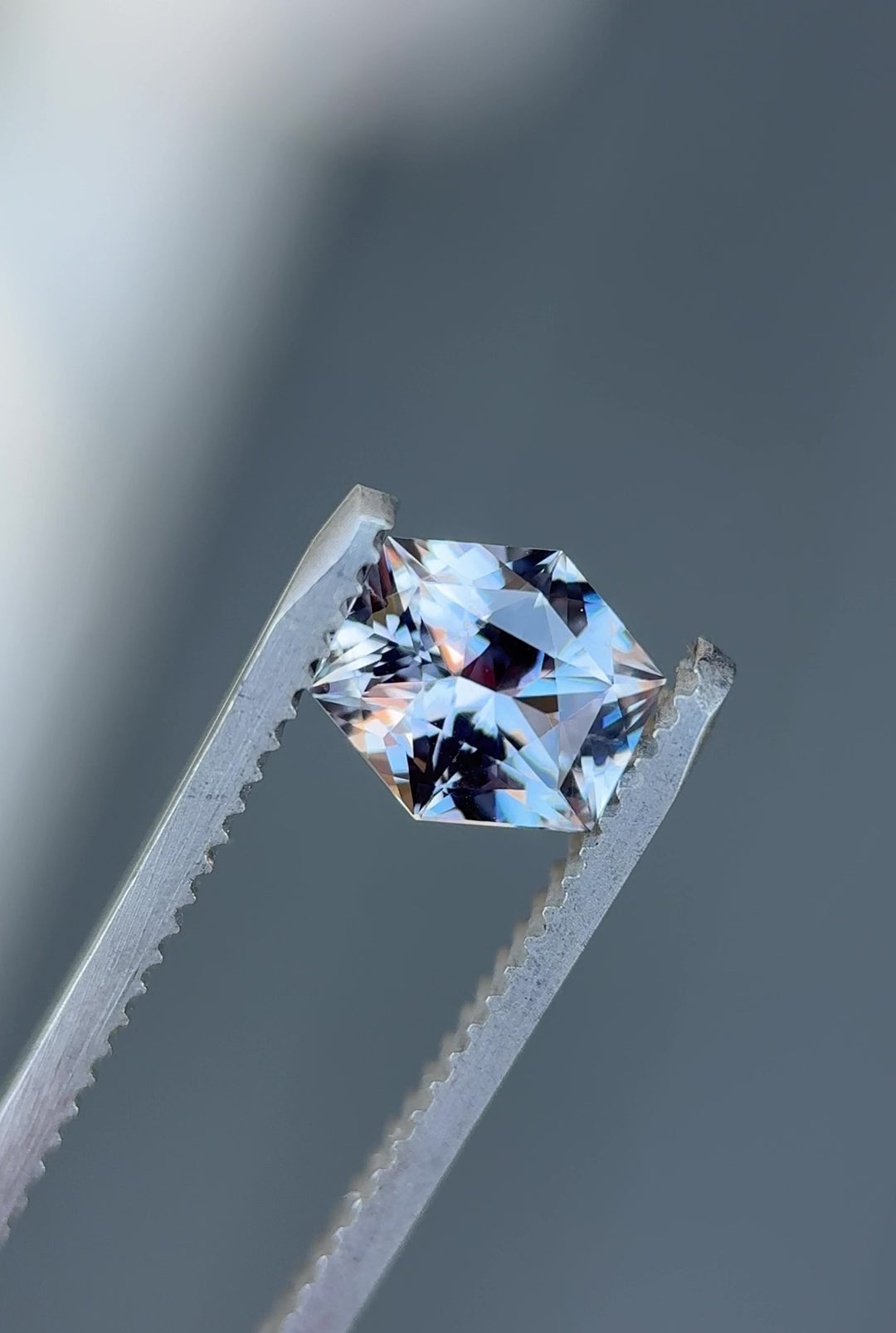 apphire in hexagonal custom cut shifting hues from grey to purple as tweezers rotate under soft light