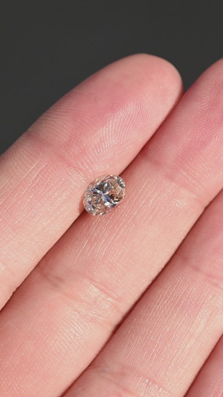 1.01ct champagne c3 oval brilliant cut diamond held in fingertips under direct sunlight rotating to show size and sparkle.