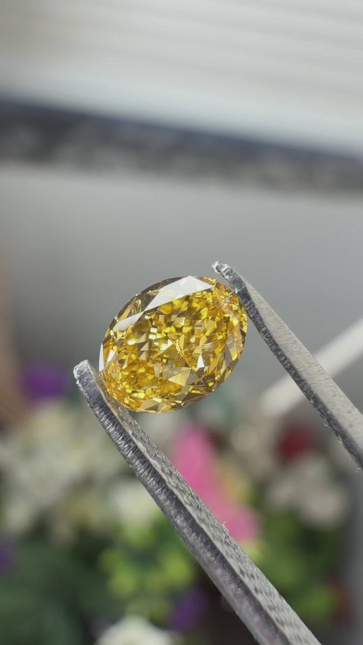 Loose natural fancy orange diamond in an oval cut held in gem tweezers under natural light.