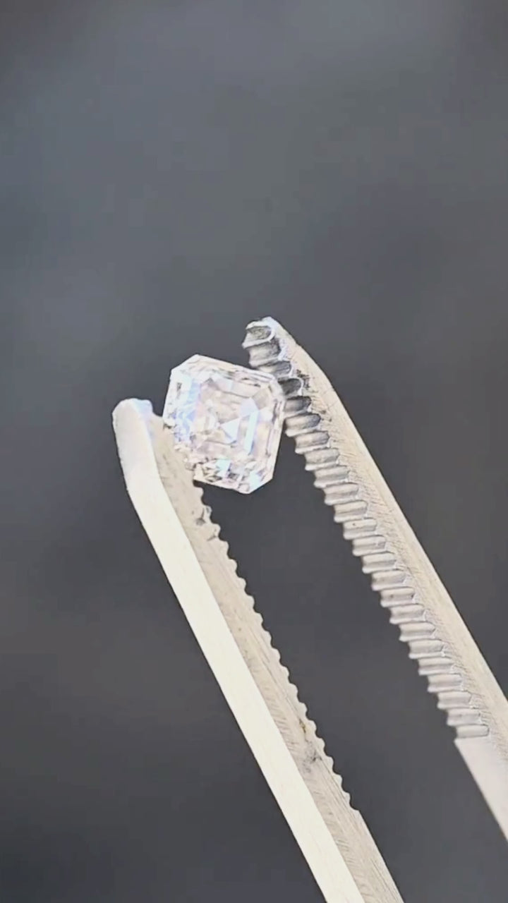 Natural 1.01 carat Canadian Asscher cut diamond rotated between jeweler’s tweezers, revealing its clipped corners, geometric symmetry and hall-of-mirrors facet pattern.