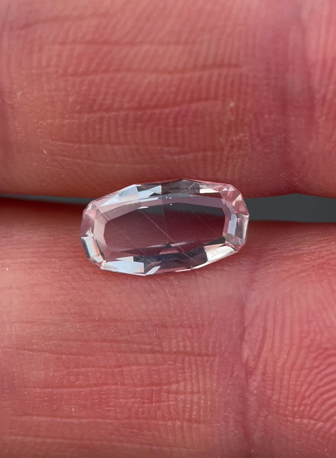 A video showcasing the intricate facets and elegant elongated step cut of a 2.03-carat peach sapphire, capturing its luminous peach tones from various angles.