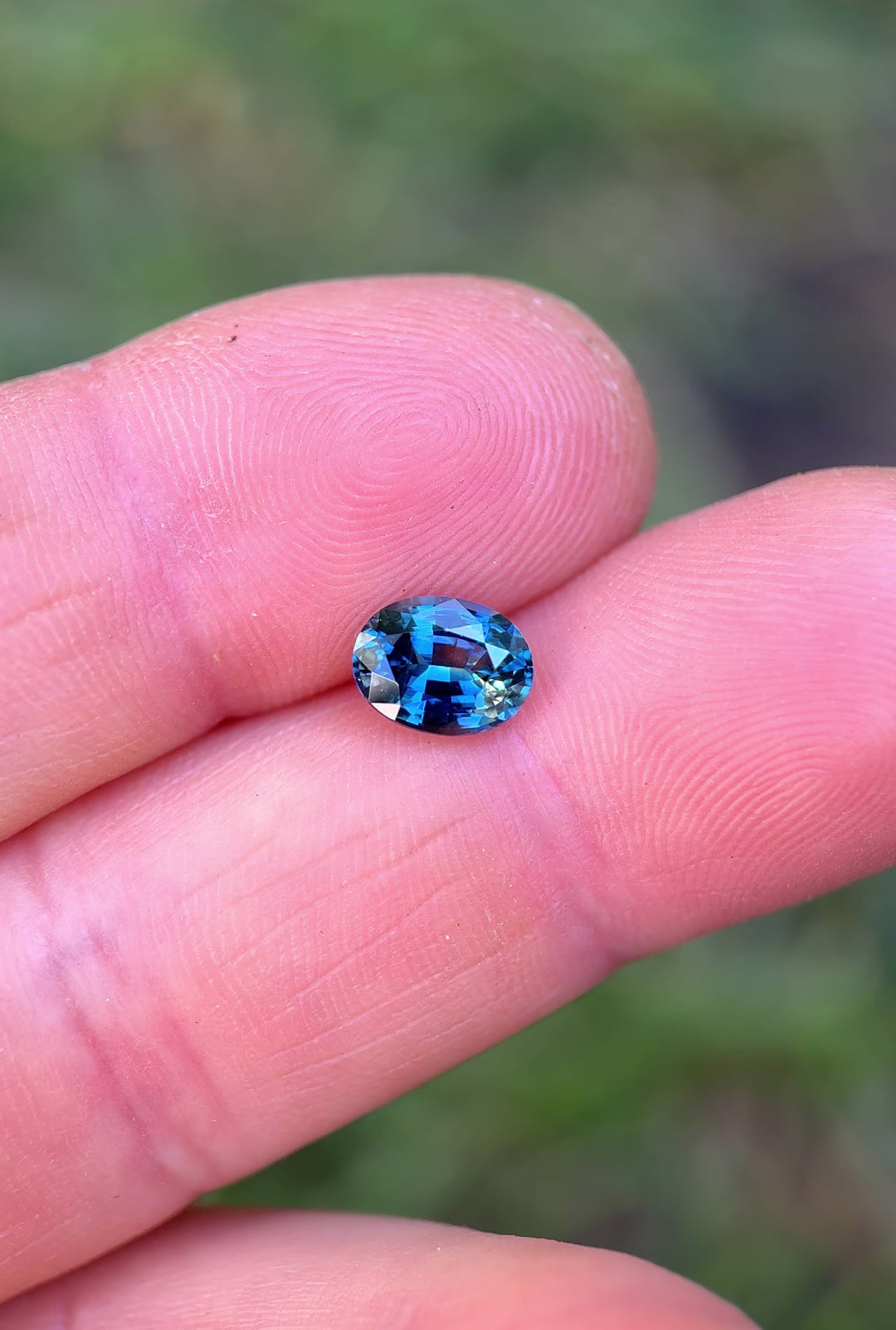 Close-up video of 1.55 carat parti sapphire resting on fingertips, capturing the gem’s vivid teal, yellow, and blue hues and the sparkle of its precision oval mixed cut, untreated sapphire from Madagascar.