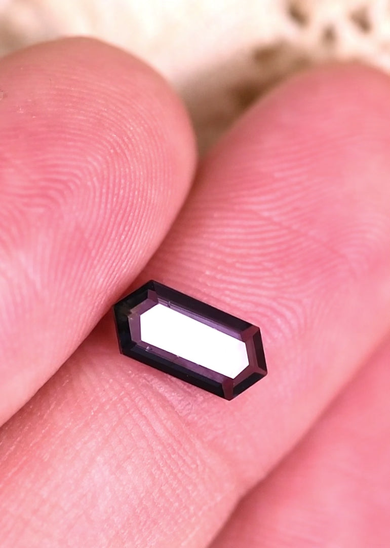Close-up video of 0.82 carat Sri Lanka spinel on hand, pink and purple tones shifting under light in a geometric hexagonal step cut portrait