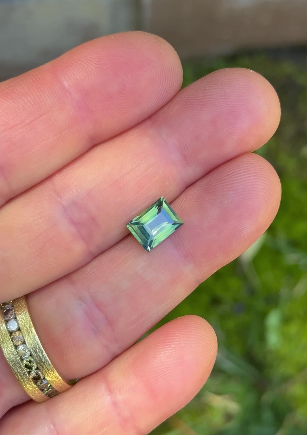 2.53ct opalescent teal blue green sapphire rotating in hand, revealing shifting oceanic tones and precision step-cut reflections.