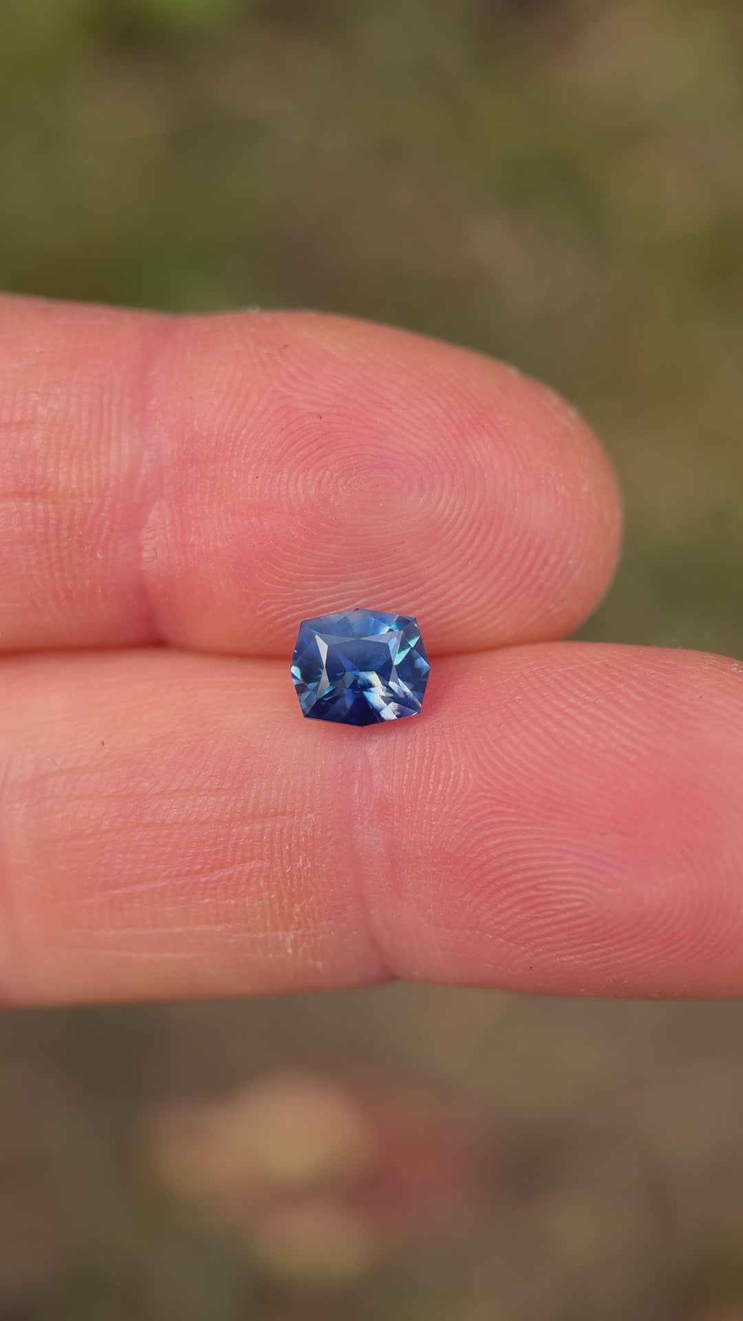 Hand-held movement video of an unheated 1.60ct Madagascar parti sapphire, capturing shifting sky-denim and royal-blue tones in the geometric cushion cut as the gem catches natural light.