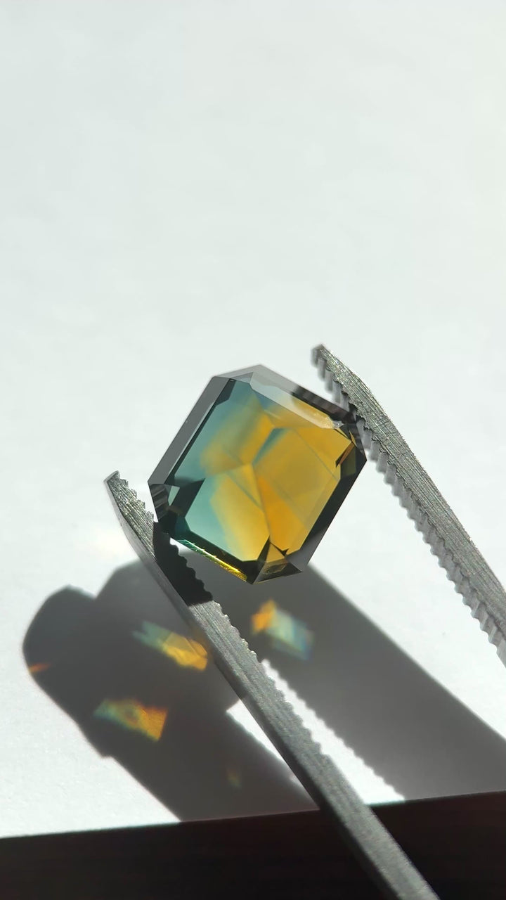 High-resolution video of a 9.14ct Nigerian parti sapphire emerald cut, filmed face-up to highlight strong orange, yellow, blue, and green color zoning, clarity, and depth from Gombe, Nigeria