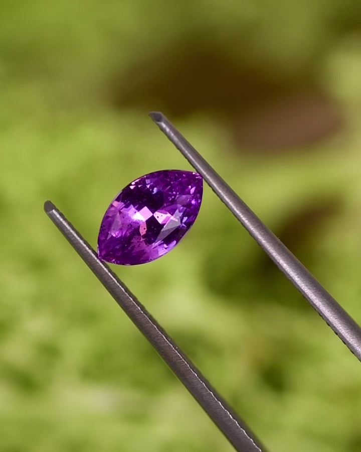Rotation video of 1.01CT purple pink sapphire held in tweezers, revealing vivid color shifts and reflections through its marquise brilliant cut, natural untreated gemstone from Sakaraha, Madagascar.