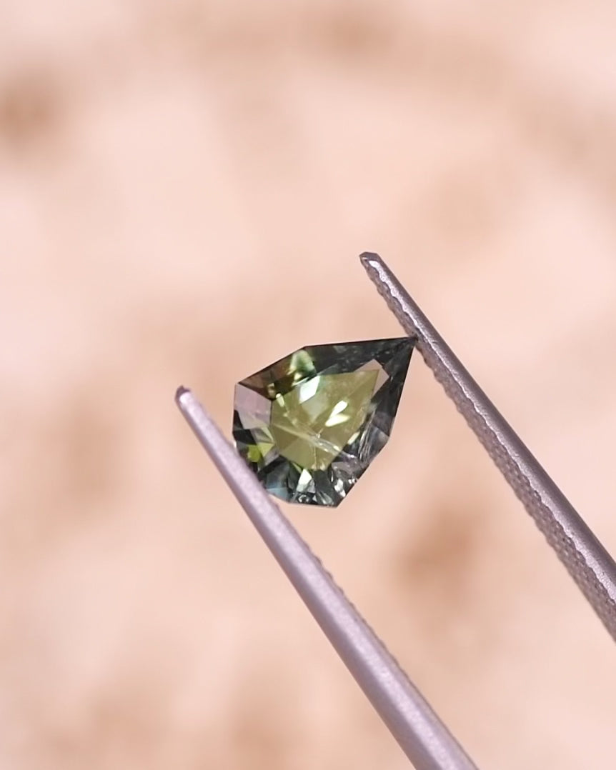 Video of 1.64CT tanzanite rotating in tweezers under natural light, revealing flashes of teal, green, and yellow through the custom geometric mixed cut shield design, untreated gem from Merelani Hills, Tanzania.