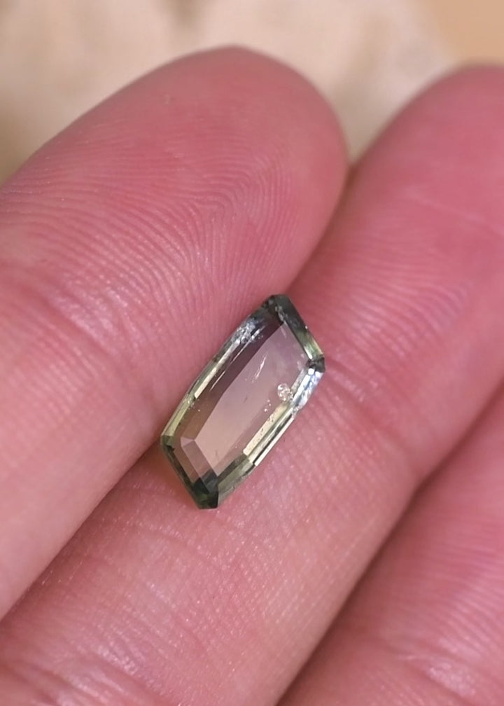 Video of a 2.31 carat natural yellow green teal sapphire rotating in hand, revealing elongated baguette portrait cut geometry, step-cut reflections, and untreated Umba River origin