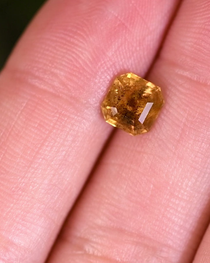 Macro video of 1.71 carat pepper yellow orange sapphire turning slowly, revealing fiery reflections and step-cut facets of its Asscher cut, untreated sapphire from Umba River Valley, Tanga, Tanzania.