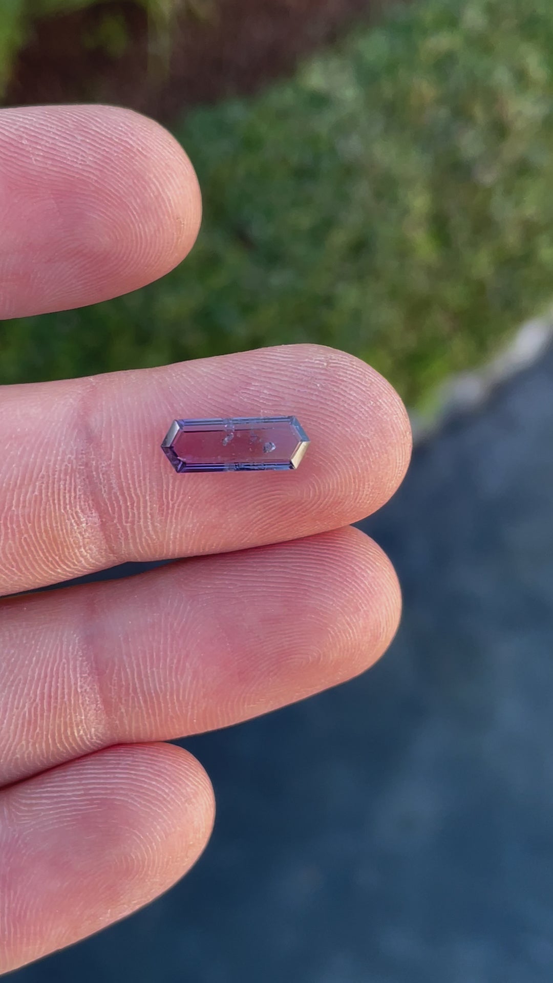 A video showcasing a sparkling hexagonal cut spinel in purple and pink shades, moving under natural light to reveal its brilliance.