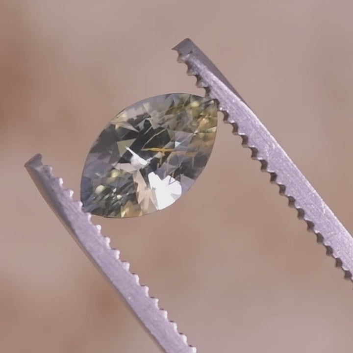 Loose marquise mixed cut sapphire from Sakaraha Madagascar rotating in tweezers, revealing the yellow, blue, and green parti color shift and faceting.