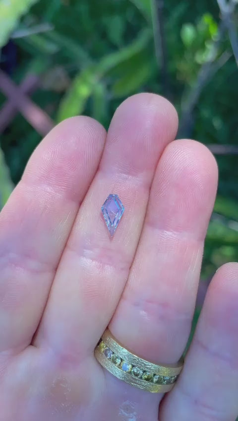 Detailed video of a 1.18-carat custom step cut portrait kite sapphire, displaying the pastel cornflower blue color and unique kite shape, set against a natural background, emphasizing its beauty and craftsmanship.