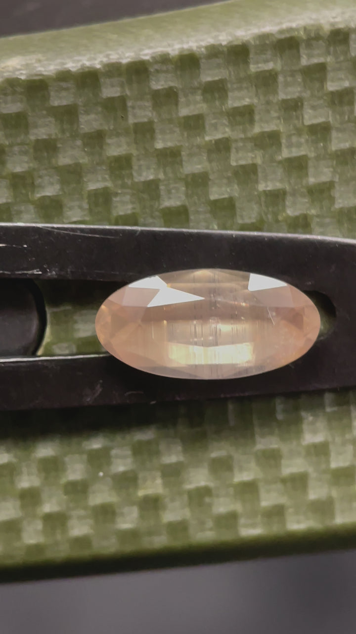 Video showcasing the unique beauty of a peach, opalescent sapphire, rotating to display its elongated oval cut and subtle color shifts in natural light.
